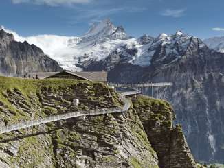Le First Cliff Walk en été, avec des visiteurs sur la passerelle, et en arrière-plan des versants verdoyants, de hautes montagnes et un ciel bleu limpide.