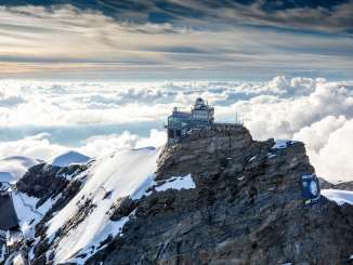 Vue aérienne du Jungfraujoch, entouré de neige, avec une mer de brouillard en arrière-plan.