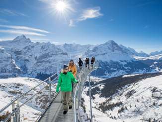 Die Touristen geniessen die winterliche Aussicht vom First Cliff Walk Aussichtspunkt. Im Hintergrund erstreckt sich der verschneite Eiger am Horizont.