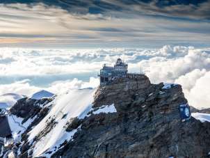 Vue aérienne du Jungfraujoch, entouré de neige, avec une mer de brouillard en arrière-plan.