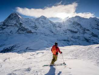 Skifahren im Skigebiet Grindelwald - Wengen. Der Skifahrer macht eine Pause und geniesst das Panorama mit Sicht auf das Dreigestirn Eiger, Mönch und Jungfrau.