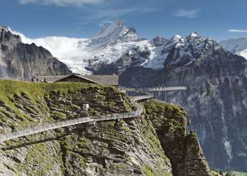 Le First Cliff Walk en été, avec des visiteurs sur la passerelle, et en arrière-plan des versants verdoyants, de hautes montagnes et un ciel bleu limpide.