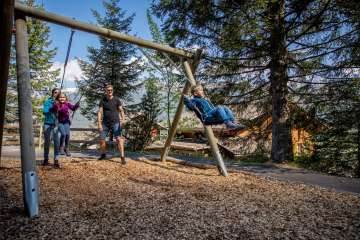 Aire de jeux de Pfingstegg : des enfants sur les balançoires, avec des adultes en arrière-plan.