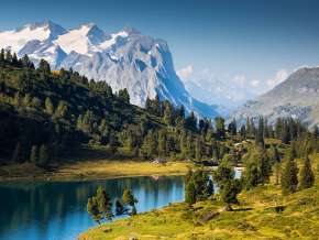 Der Engstlensee ist umgeben von grünen Wiesen und Nadelbäumen. Im Hintergrund sind die verschneiten Berggipfel zu sehen.