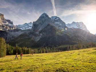 Herbstwanderung über eine Lichtung. Die Wanderer schauen sich das Bergpanorama im Rosenlauital mit den leicht verschneiten Gipfeln an.