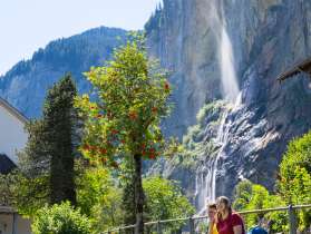 Die Wanderer machen eine wohlverdiente Pause bei der Kirche in Lauterbrunnen. Im Hintergrund ist der Staubbachfall von Sonnenstralen beleuchtet.