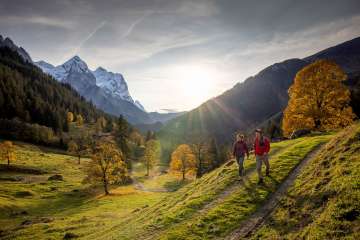 Zwei Wanderer unterwegs in der Landschaft vom Rosenlauital. Es herrscht eine herbstliche Stimmung und der Himmel ist mit leichten Dunstwolken bedeckt. Das Bergpanorama hat einen verschneiten Umhang.