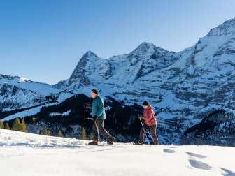 Unterwegs in der verschneiten Landschaft bei sonnigem Wetter mit den Schneeschuhen. Der Schneeschuhtrail in Mürren bietet eine einmalige Sicht auf Eiger, Mönch und Jungfrau.