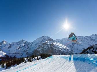 Ein Skifahrer auf der Skicrosspiste im Skigebiet Mürren-Schilthorn. Das Dreigestirn Eiger, Mönch und Jungfrau ist aus der Ferne zu sehen.