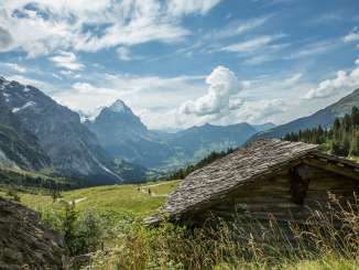 Mitten in einer grünen Wiese steht eine kleine Alphütte auf der Schwarzwaldalp. Die Aussicht reicht bis zum Eiger. Die Wanderer geniessen das schöne Wetter.