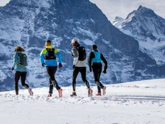 Deux coureurs lors d'une course de trail hivernale à Grindelwald First, avec l'Eiger en arrière-plan.