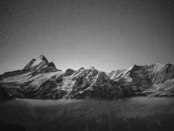 Photo en noir et blanc du sommet la nuit, avec un ciel étoilé et un panorama montagneux.