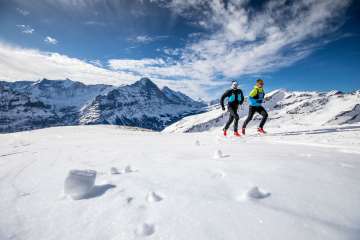 Deux coureurs lors d'une course de trail hivernale à Grindelwald First, avec l'Eiger en arrière-plan.